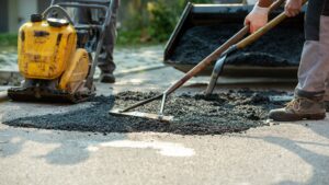 Low angle view of two workers arranging fresh asphalt mix with rakes and shovel