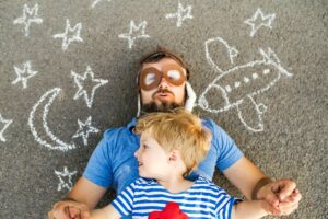 Portrait of mature man wearing pilot hat and his little son lying on asphalt painted with airplane,