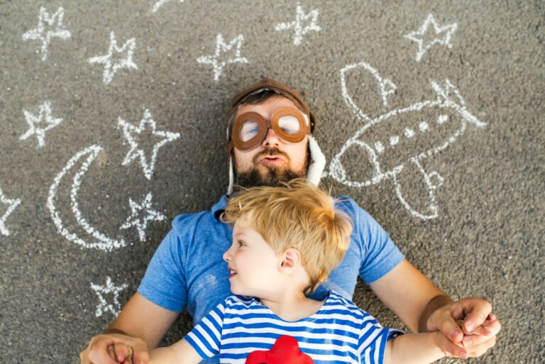 Portrait of mature man wearing pilot hat and his little son lying on asphalt painted with airplane,