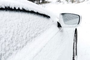 Snow layer on rearview mirror, windshield, window of sedan, car in backyard driveway parking lot