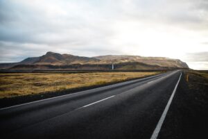 Beautiful view of an asphalt road way with green meadows, rocky hills against a light horizon sky
