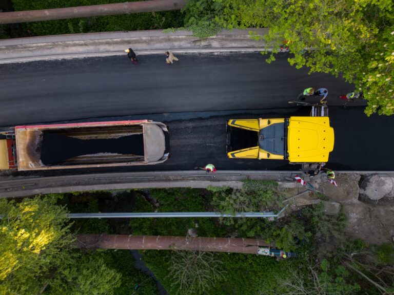 Aerial view of the construction of a new road as asphalt pavers, rollers, machinery, and workers