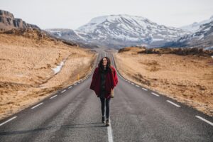 happy young woman walking on asphalt road in iceland, hvalfjardarvegur
